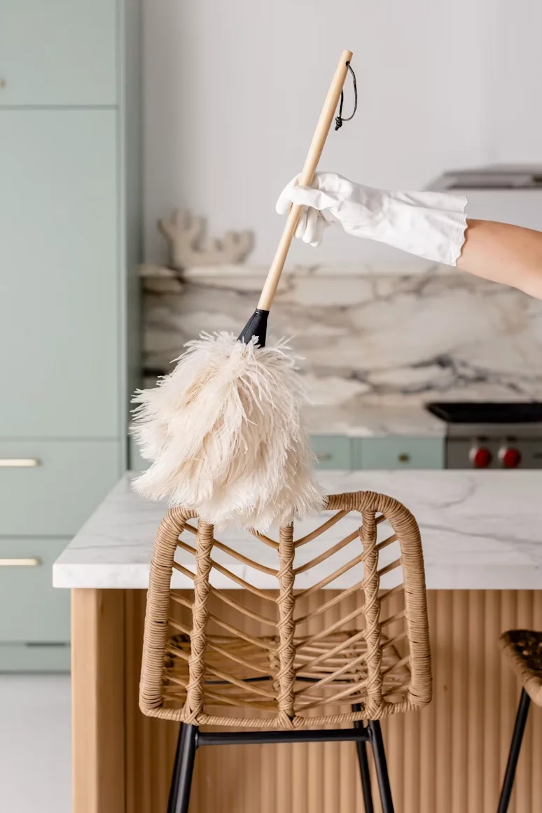 Gloved hand dusting a woven bar stool beside a marble kitchen island in a Nashville home
